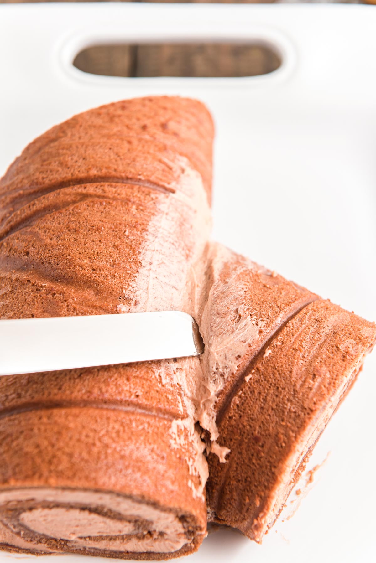 A small piece of cake roll being attached to the larger roll with buttercream to make a yule log cake.