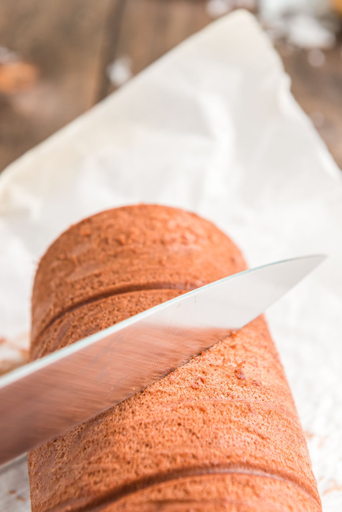 A knife cutting a diagonal slice in a chocolate cake roll for a buche de noel.