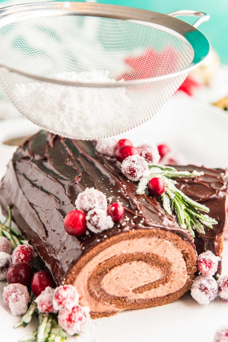 A Buche de Noel yule log cake getting powdered sugar dusted over the top of it.