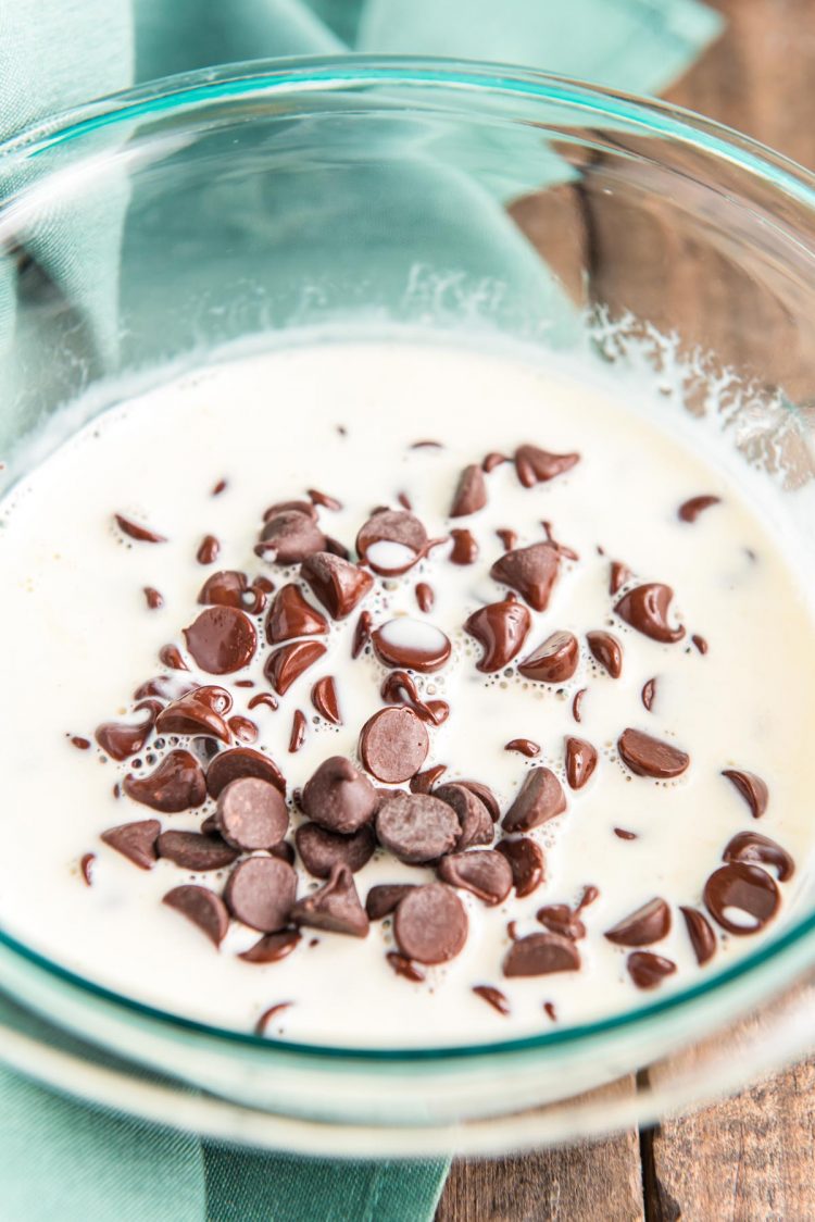 Chocolate chips and warm heavy cream in a glass bowl melted to make ganache.