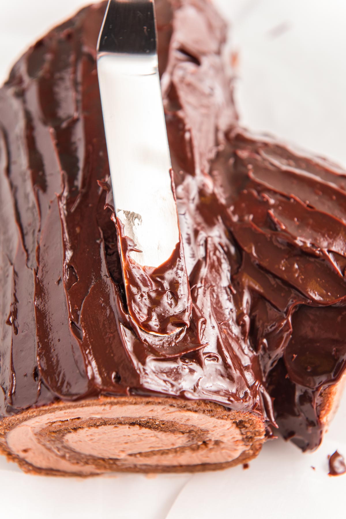 Chocolate ganache being spread over the top of a cake roll to make a buche de noel yule log cake.