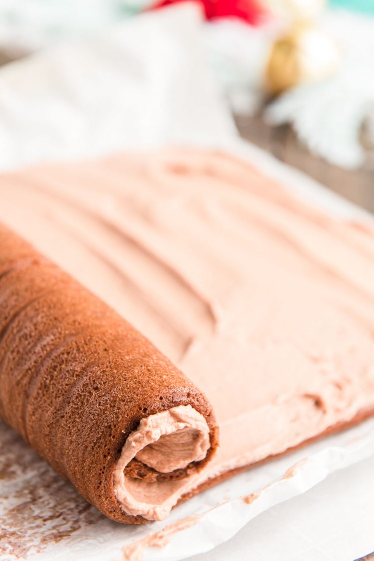 Chocolate cake roll being rolled up with frosting in it to make a buche de noel.