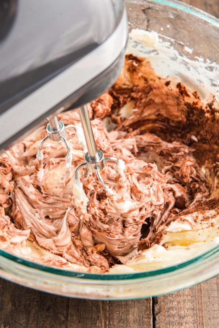 Chocolate buttercream being made in a glass bowl with a hand mixer.