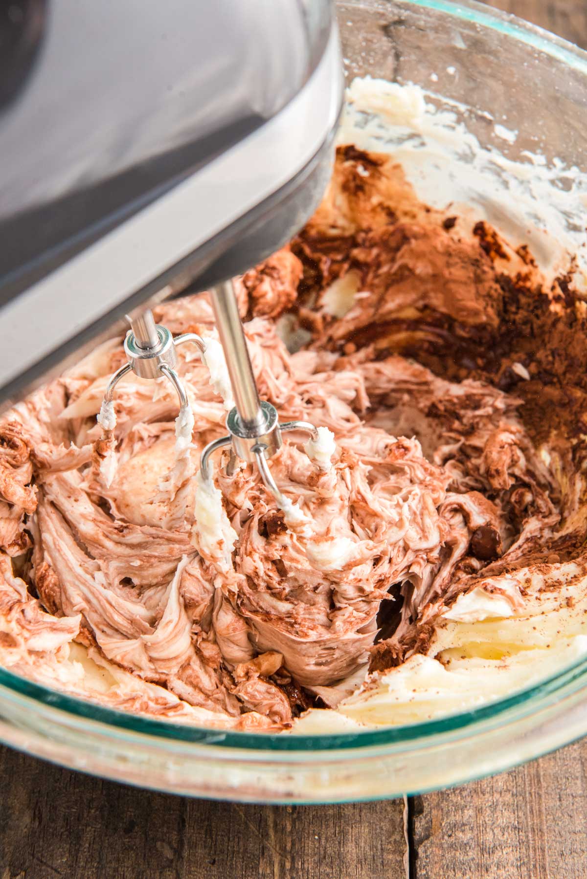 Chocolate buttercream being made in a glass bowl with a hand mixer.