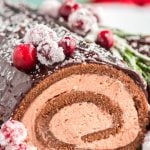 Close up photo of a buche de noel yule log cake with chocolate filling topped with cranberries and rosemary.