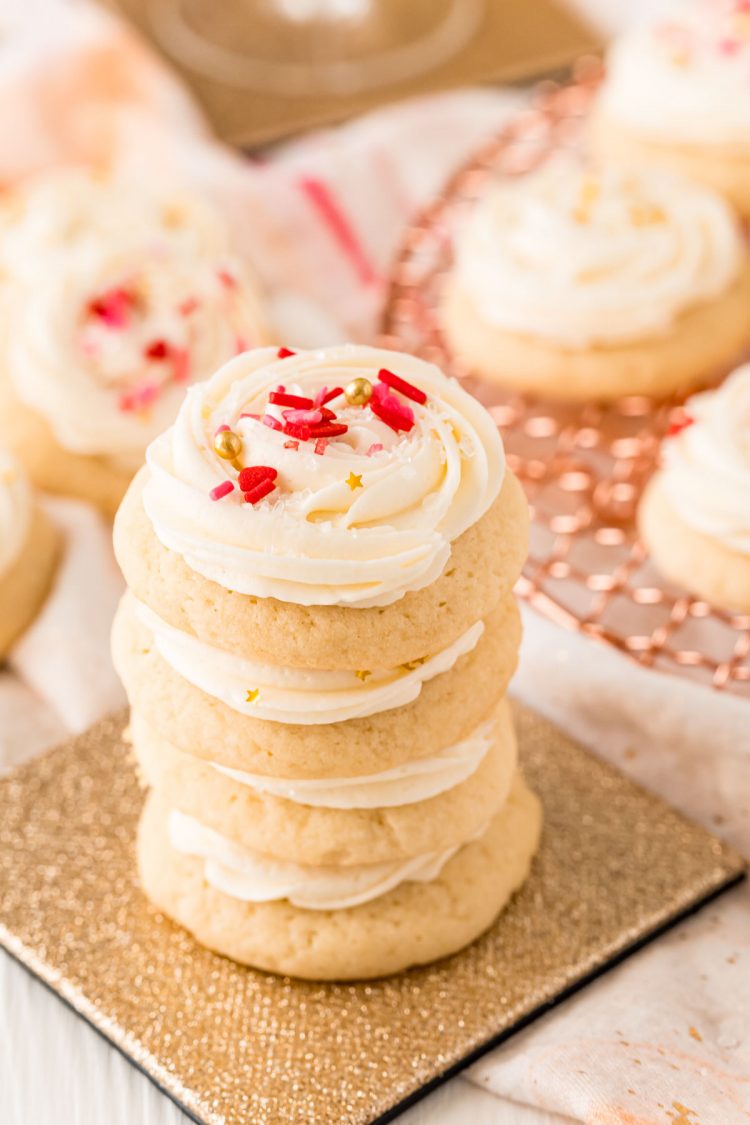 A stack of champagne sugar cookies topped with white frosting and valentine's sprinkles on a glitter coaster.