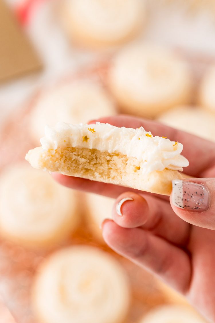 A woman's hand holding a sugar cookie with a bite taken out of it.