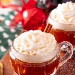 Close up photo of coffee in a small rounded mug topped with whipped cream and cinnamon and garnished with a cinnamon stick.