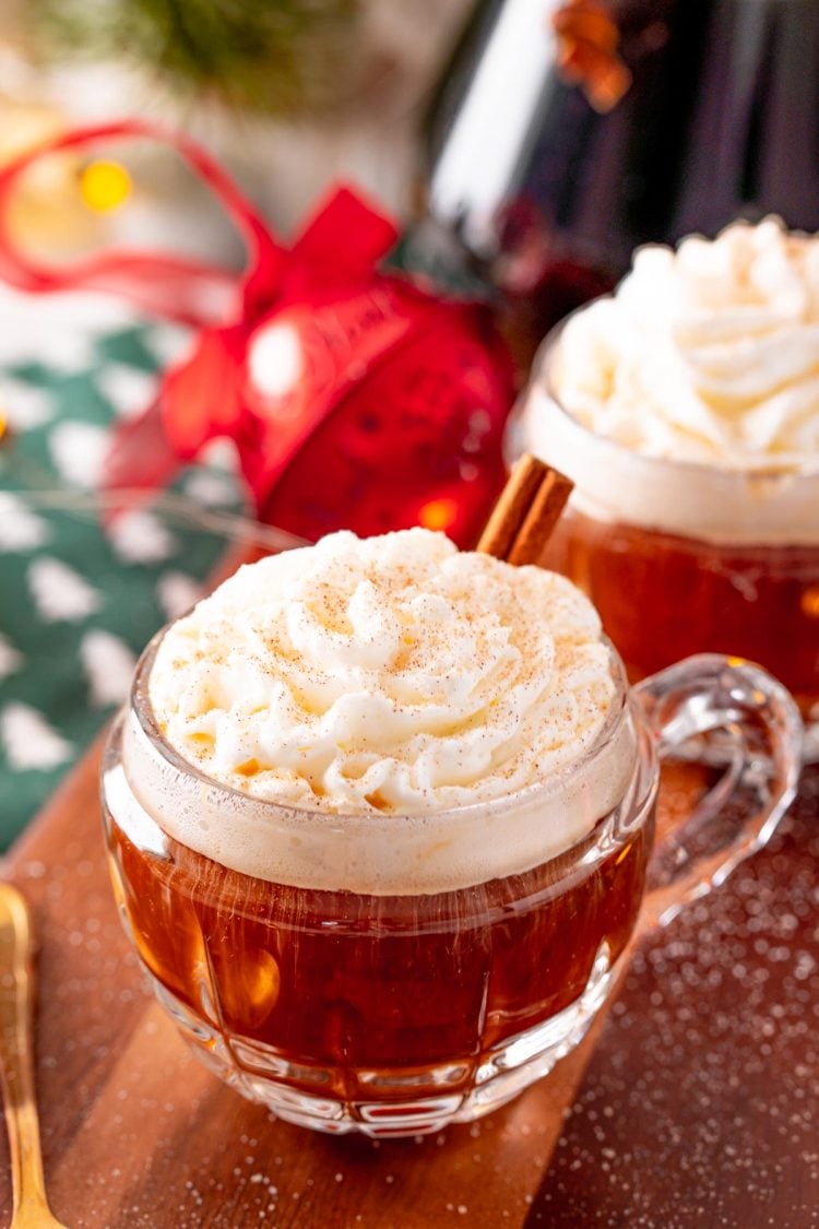 Close up photo of coffee in a small rounded mug topped with whipped cream and cinnamon and garnished with a cinnamon stick.