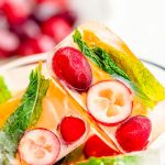 Close up photo of ice cubes with cranberries, orange, and mint in them