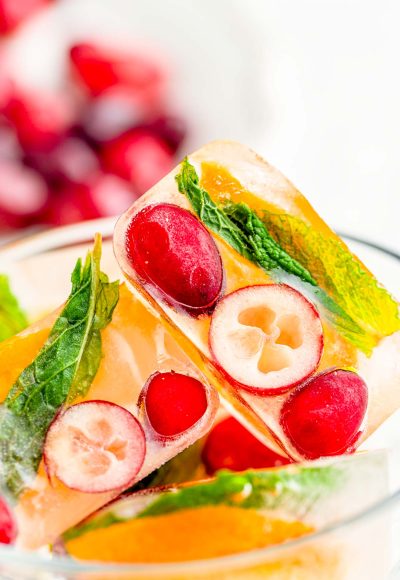 Close up photo of ice cubes with cranberries, orange, and mint in them