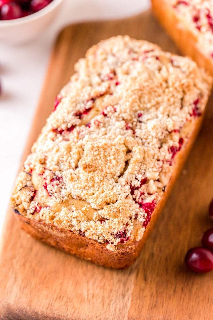 Close up photo of a loaf of cranberry quick bread on a wooden cutting board.