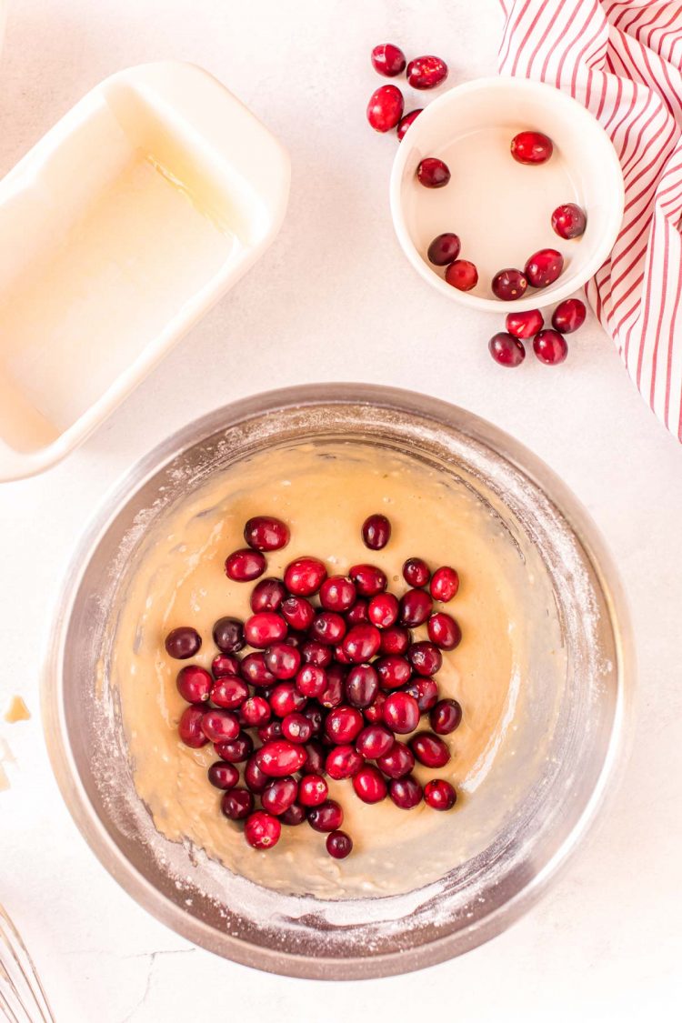 Cranberries being folded into batter in a metal mixing bowl.