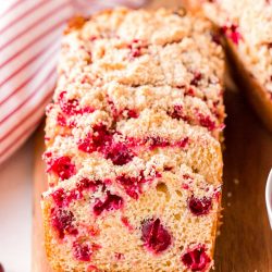Close up photo of slices of cranberry bread resting on each other on a wooden cutting board.