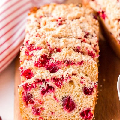 Close up photo of slices of cranberry bread resting on each other on a wooden cutting board.