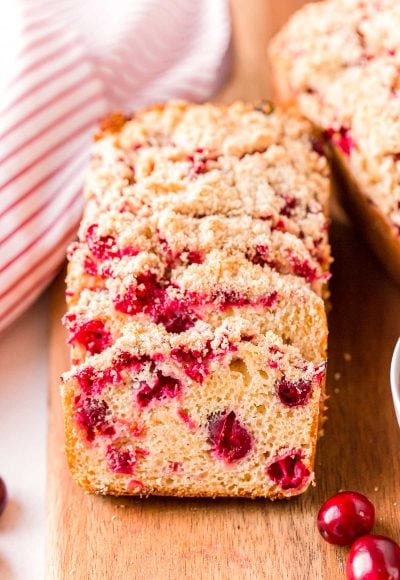 Close up photo of slices of cranberry bread resting on each other on a wooden cutting board.