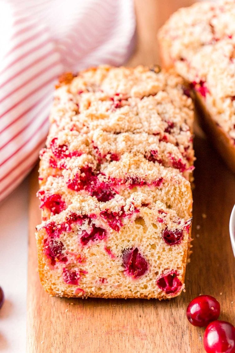 Close up photo of slices of cranberry bread resting on each other on a wooden cutting board.