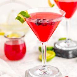 A cosmopolitan martini on a stone coaster garnish with lime rind.