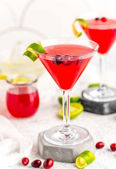 A cosmopolitan martini on a stone coaster garnish with lime rind.