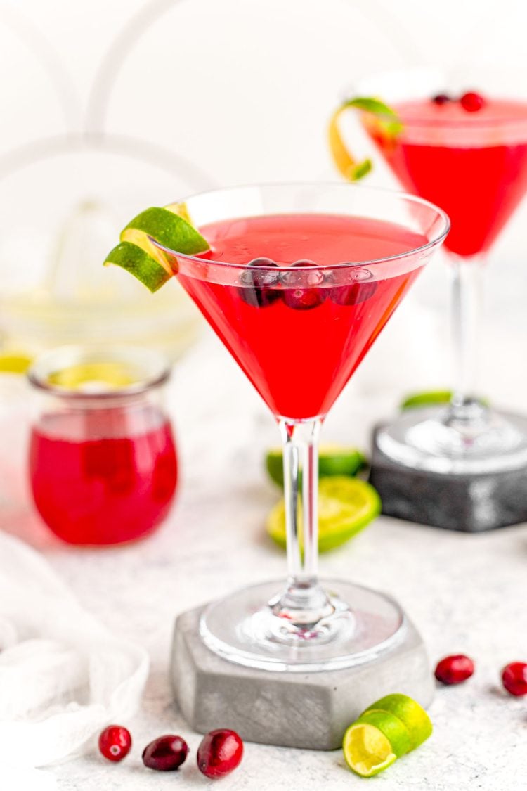 A cosmopolitan martini on a stone coaster garnish with lime rind.