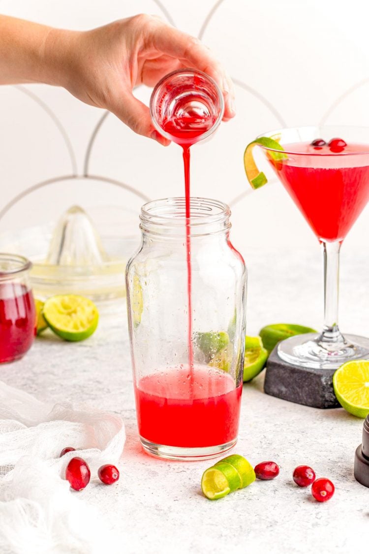 Cranberry simple syrup being poured into a glass cocktail shaker.