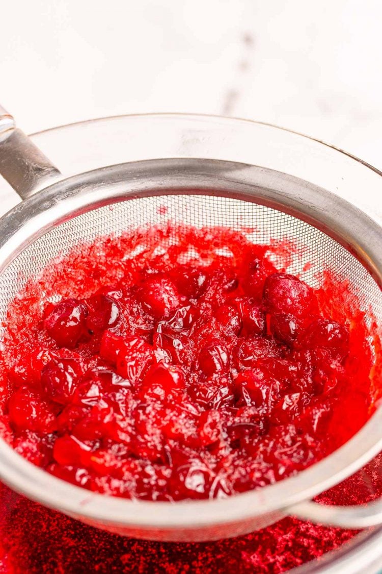 Cranberries being run through a fine mesh strainer.