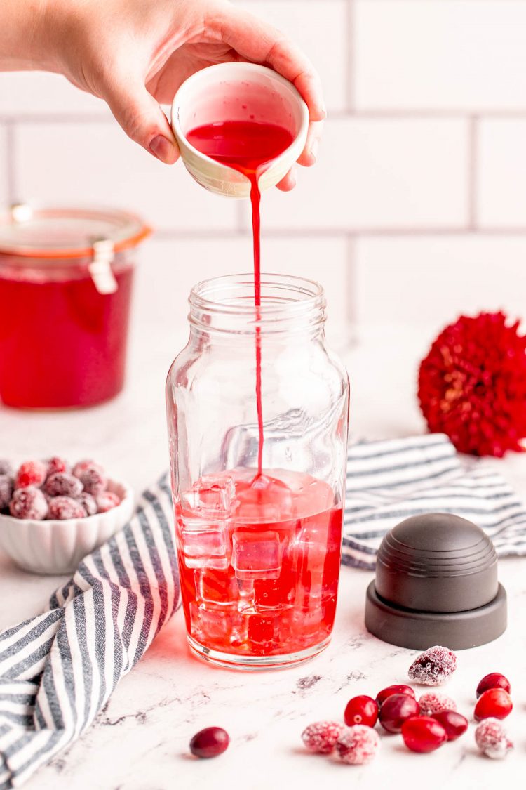 Cranberry simple syrup being poured into a cocktail shaker.
