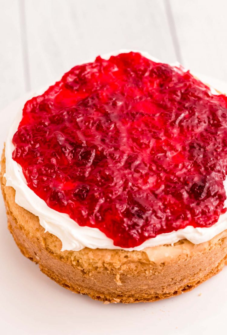 A round cake layer being topped with frosting and cranberry compote.