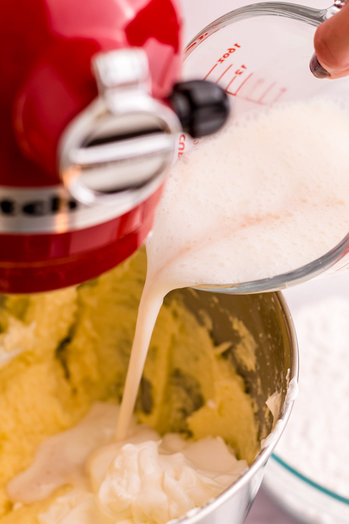 Buttermilk being added to cake batter in a stand mixer bowl.