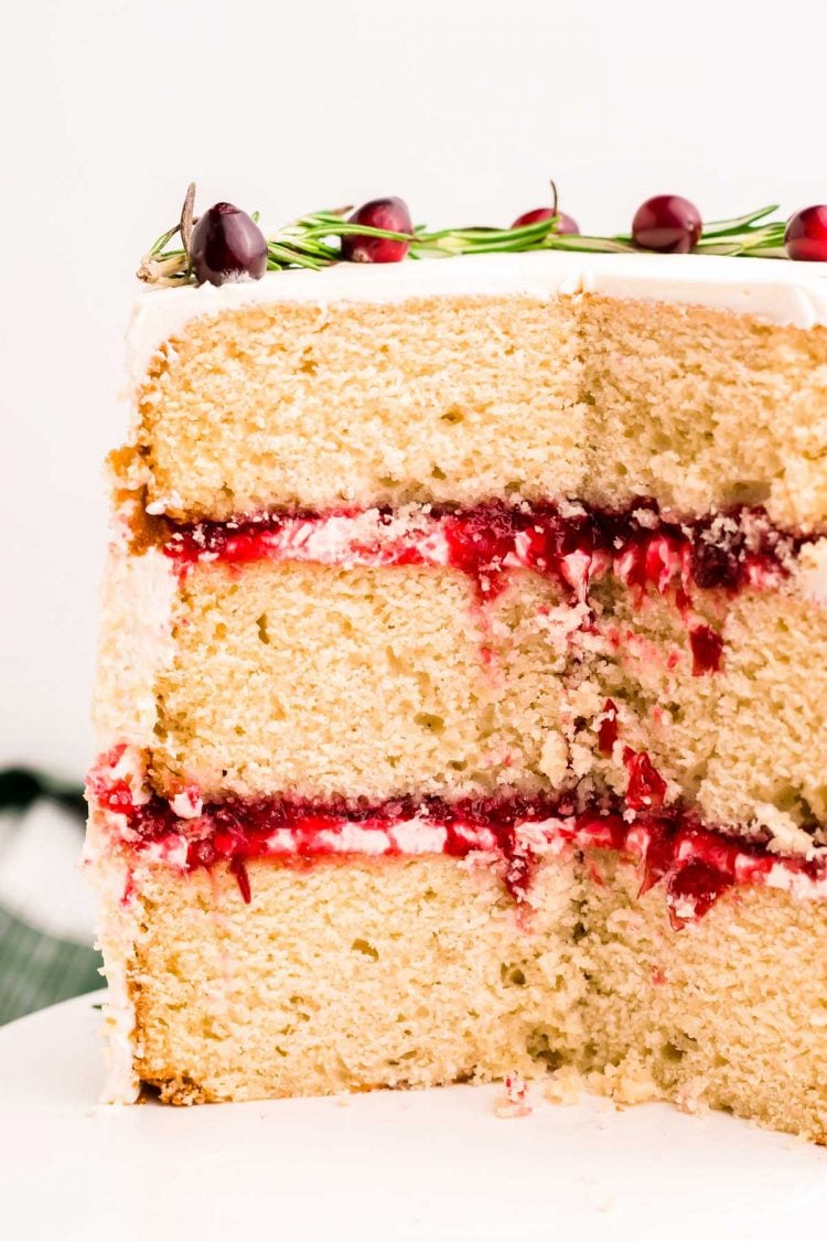 A three-layer cake with cranberry filling and white chocolate frosting that has been cut into to reveal the layers.