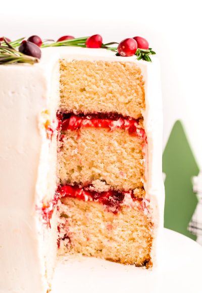 A three-layer cake with cranberry filling and white chocolate frosting that has been cut into to reveal the layers.