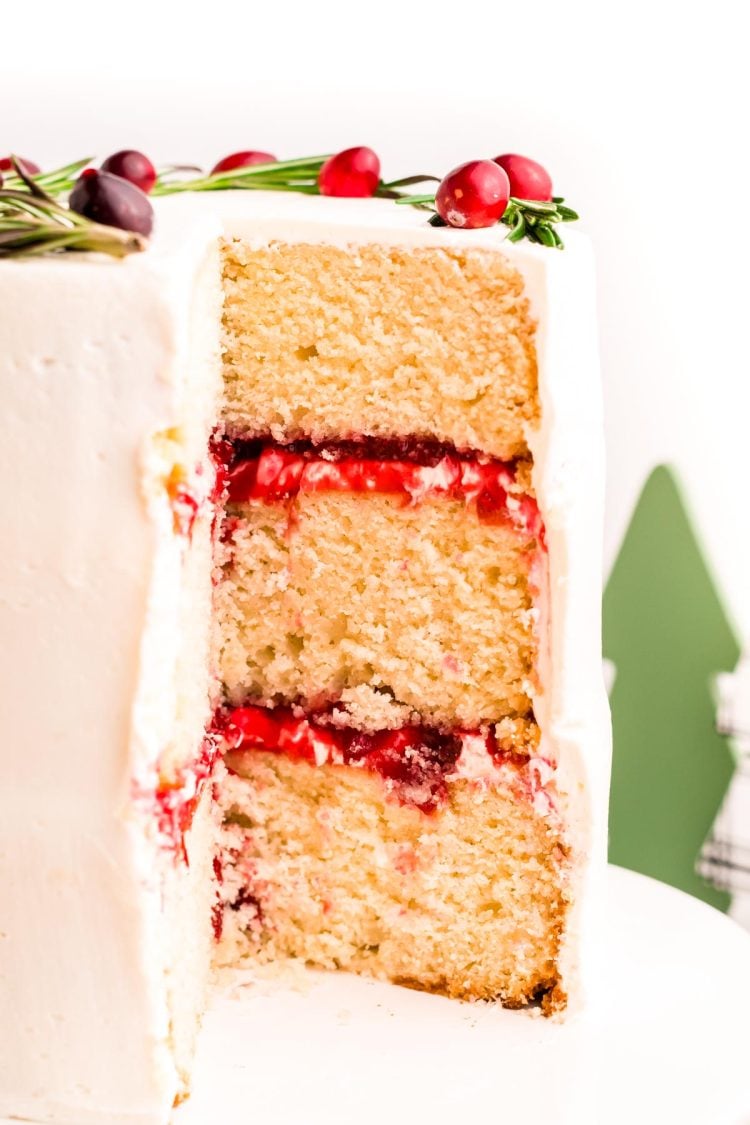 A three-layer cake with cranberry filling and white chocolate frosting that has been cut into to reveal the layers.