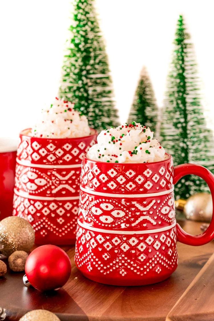 A red mug filled with eggnog hot chocolate and topped with whipped cream and christmas sprinkles.