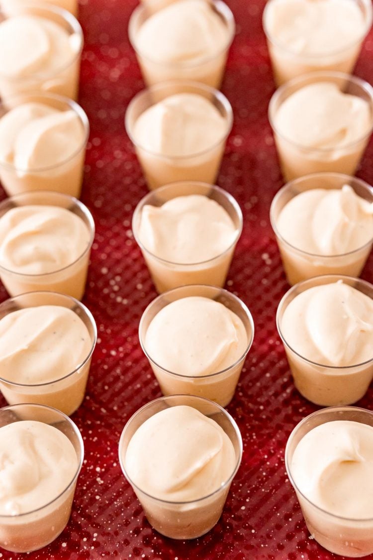 Eggnog pudding shots in plastic shot glasses on a red baking sheet.