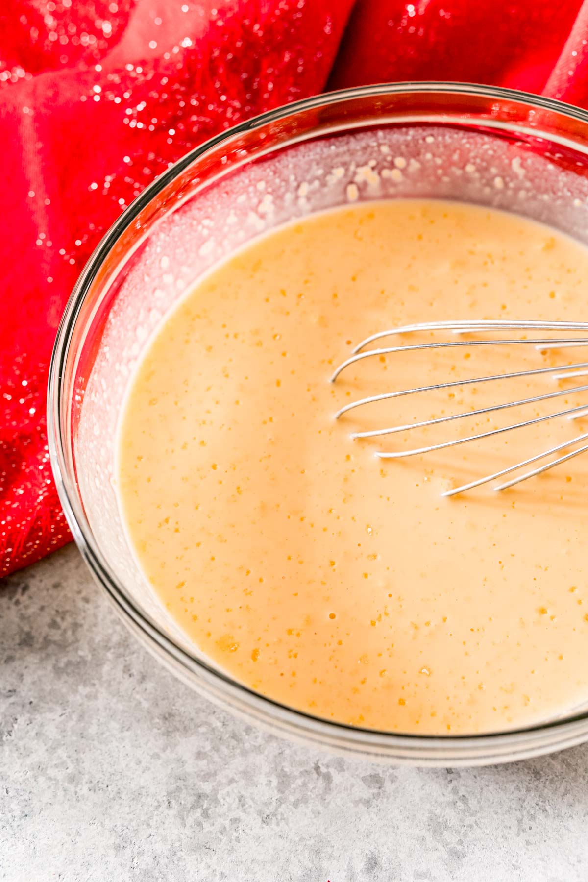 Vanilla pudding being made in a glass mixing bowl with a whisk.