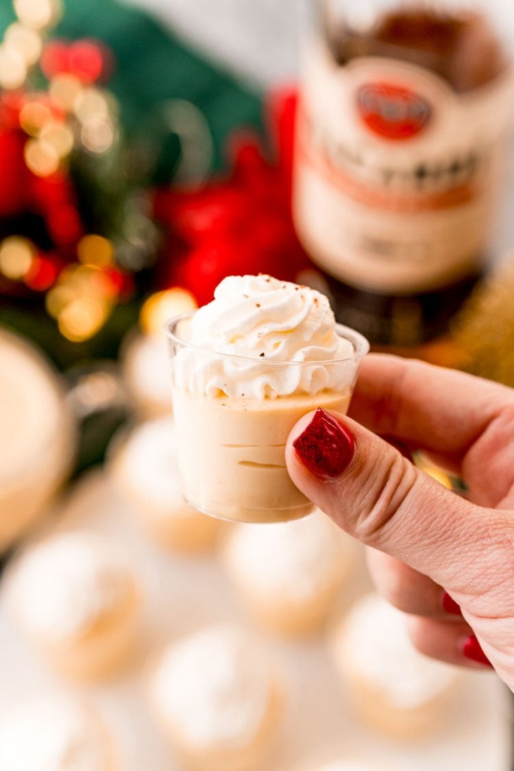 A woman's hand holding a pudding shot topped with whipped cream.