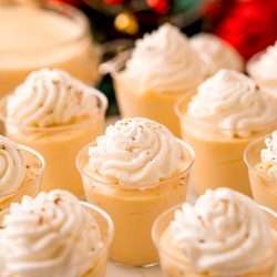 Close up photo of pudding shots topped with whipped cream and nutmeg.