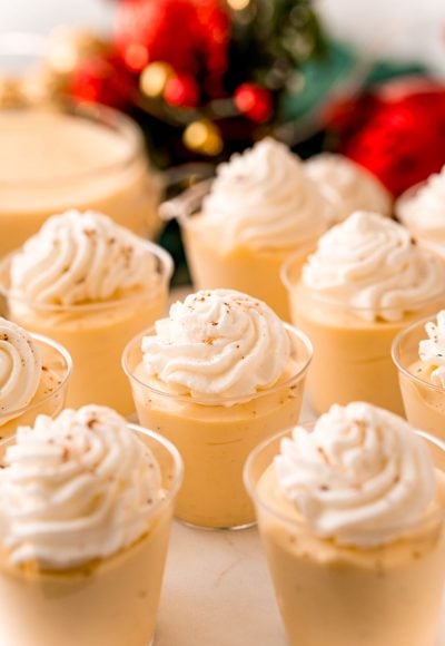 Close up photo of pudding shots topped with whipped cream and nutmeg.