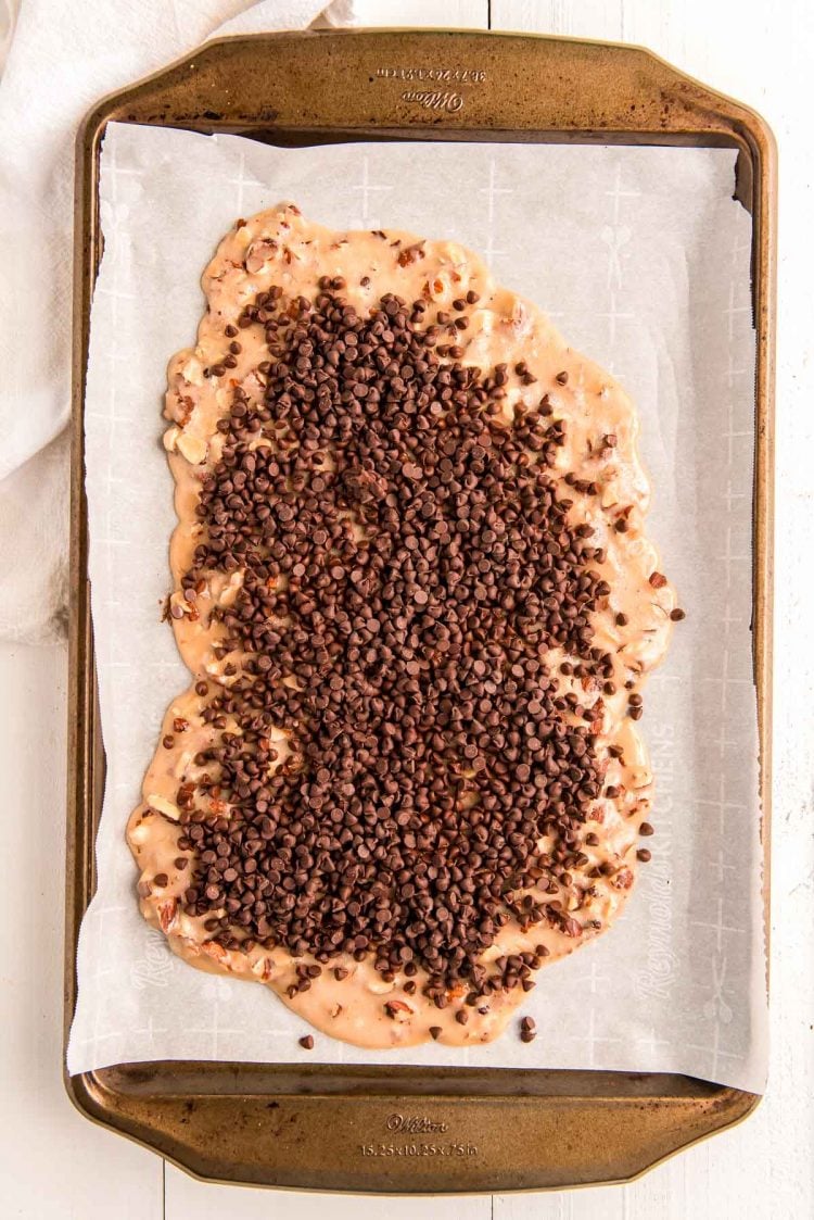 Chocolate chips sprinkled over toffee on a baking sheet.