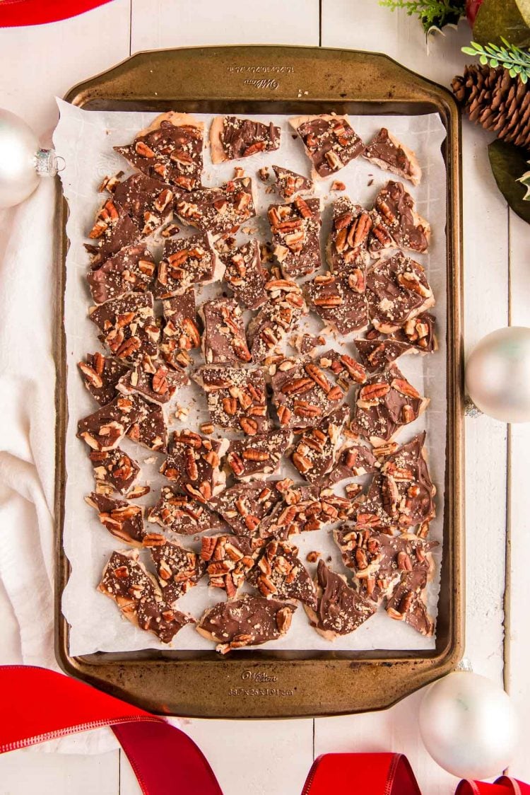 Overhead photo of cracked toffee on a baking sheet with holiday decorations around.