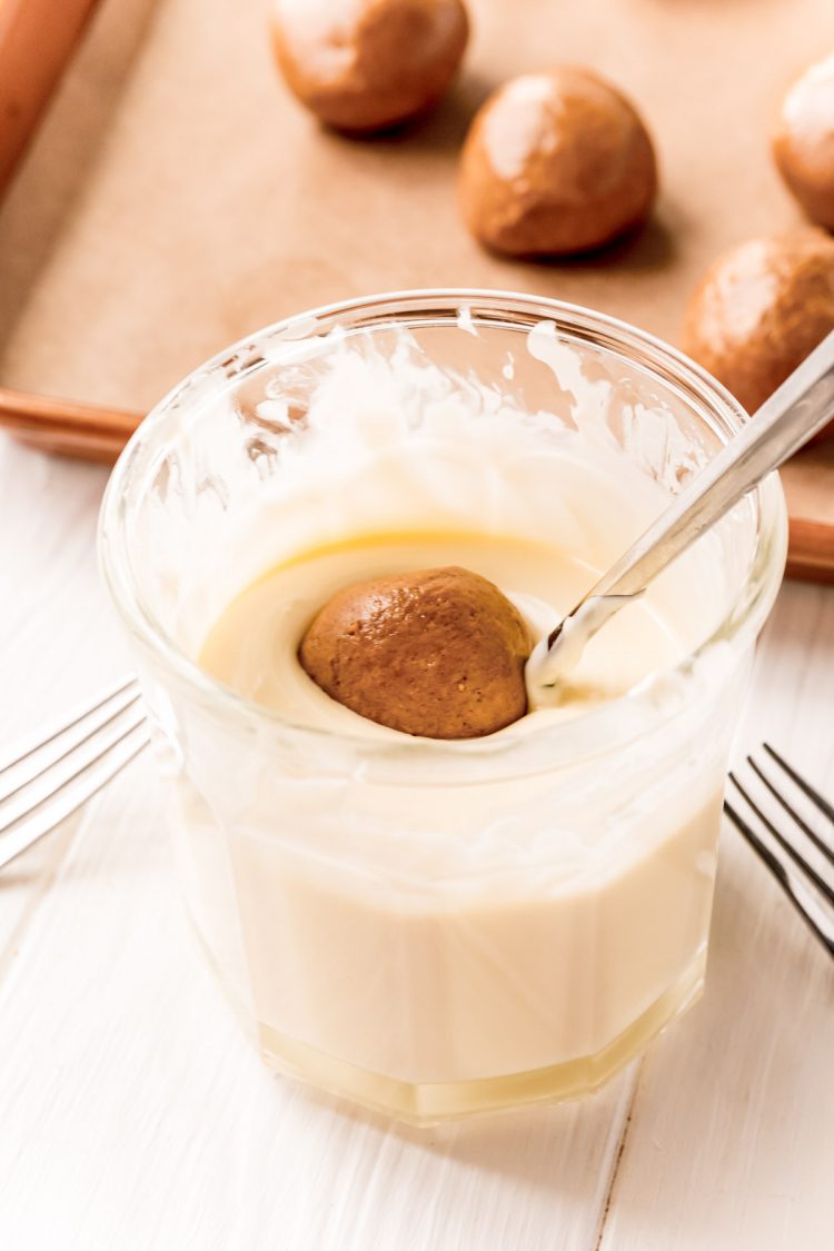 Gingerbread balls being dipped in melted white chocolate to coat.