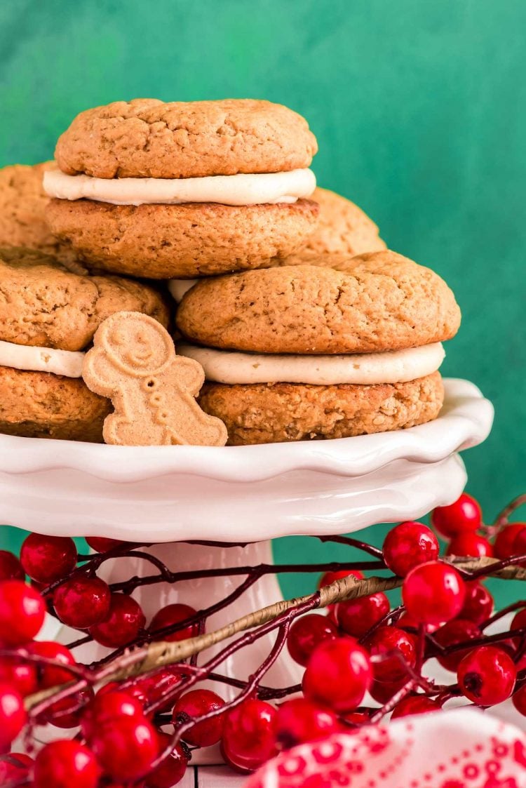 Close up photo of gingerbread flavored whoopie pies on a white cake stand with holly berries around it.