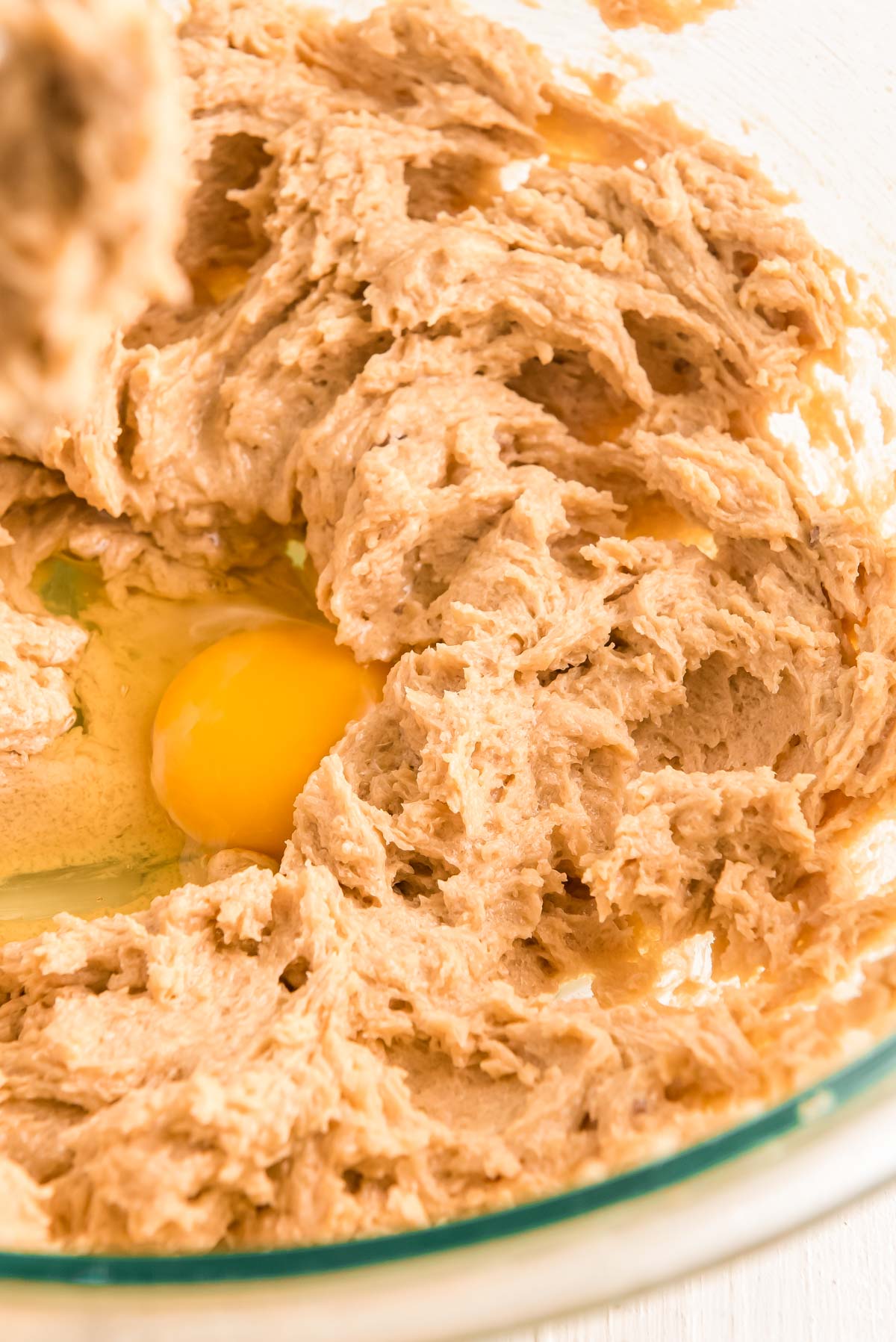 Egg being added to batter in a glass mixing bowl.