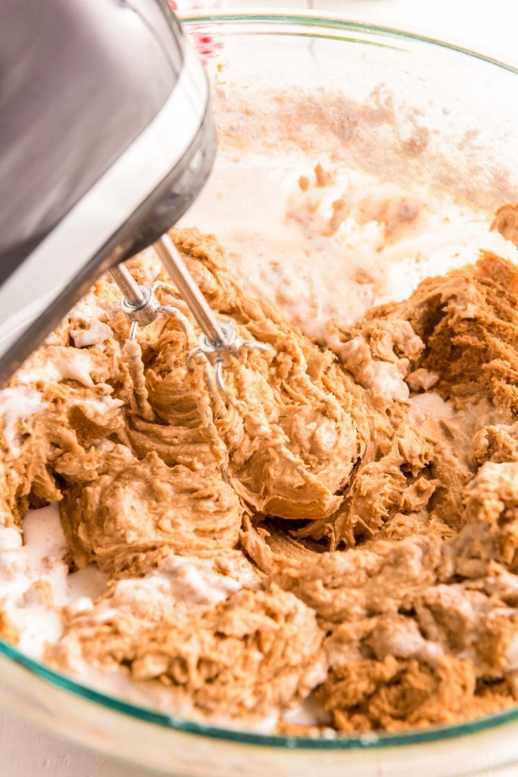 Cake batter being mixed in a glass mixing bowl with a hand mixer.