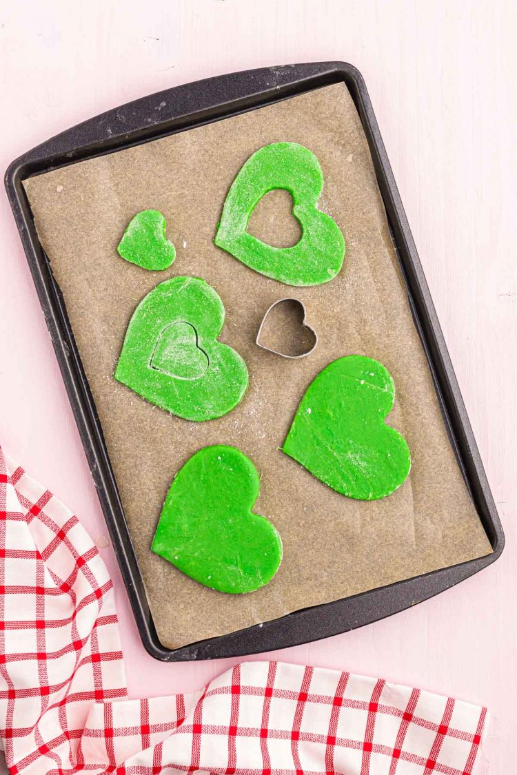 Green heart shaped cookies on a parchment-lined baking sheet.