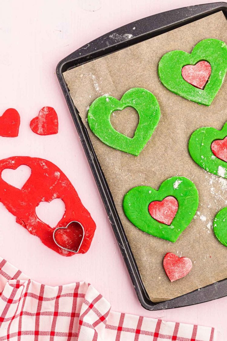 A heart cookie cutter with red and green heart-shaped cookie dough.