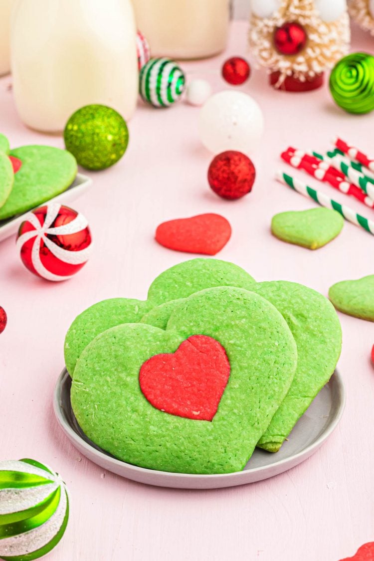 Heart shaped Grinch Cookies inspired by the movie on a plate with holiday decorations in the background.