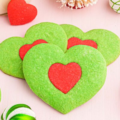 Close up photo of green heart shaped cookies with a red heart in the center inspired by the Grinch.