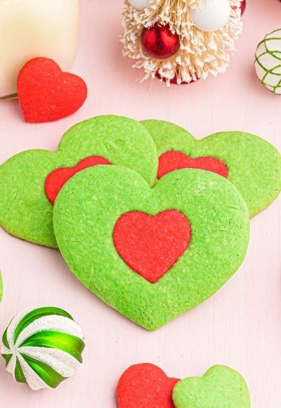 Close up photo of green heart shaped cookies with a red heart in the center inspired by the Grinch.