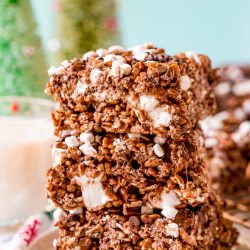 Close up photo of 3 chocolate rice krispie treats stacked on top of each other on a white plate.